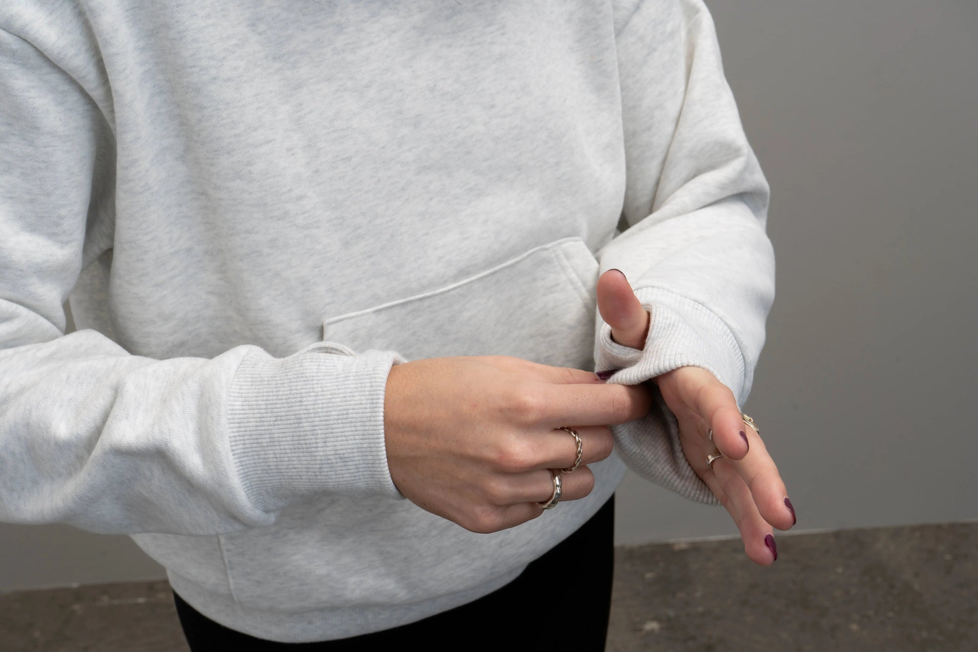 En person iført en Hugz tyngde hoodie står afslappet med hænderne i lommerne, hvilket fremhæver de integrerede stressbolde i ærmerne. Designet giver en beroligende taktil oplevelse, der hjælper med at reducere stress og øge fokus.